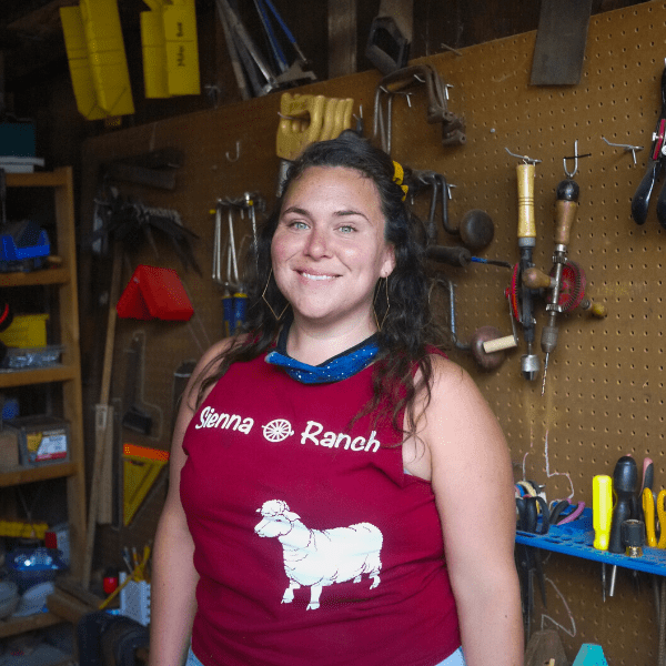 A woman in a red shirt standing in front of a tool shed.