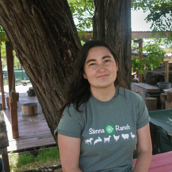 A woman sits on a bench under a tree wearing a t - shirt that says sana farm.