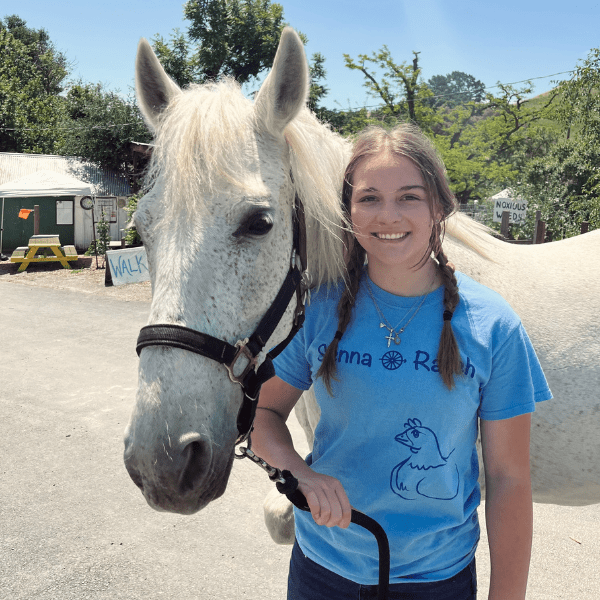 A girl standing next to a white horse.